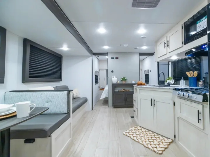 Modern RV rental interior with bright kitchen, cozy dinette, and wood-look flooring, extending to a bedroom.. Coachmen Shasta 2027