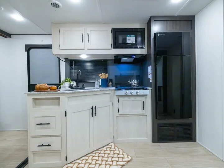 Modern RV rental kitchen featuring light cabinets, dark appliances, a sink, stove, and a spacious refrigerator.. Coachmen Shasta 2027