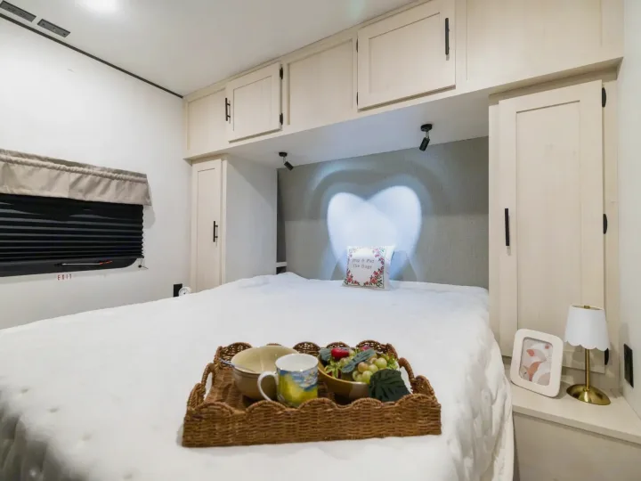 Cozy RV rental bedroom with breakfast in bed, heart-shaped light, overhead storage, and an exit window.. Coachmen Shasta 2027