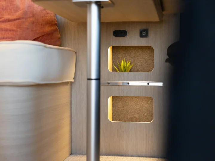 Cozy RV rental interior: modern table, cushion, convenient power outlets, and lighted wall niches, one with an artificial plant.. Noovo Noovo Next 2026