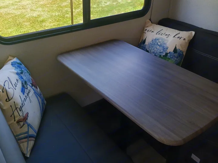 Enjoy the cozy dinette inside this rv rental, featuring comfy seating, decorative pillows, and a scenic outdoor view.. Forest River Shasta 2021