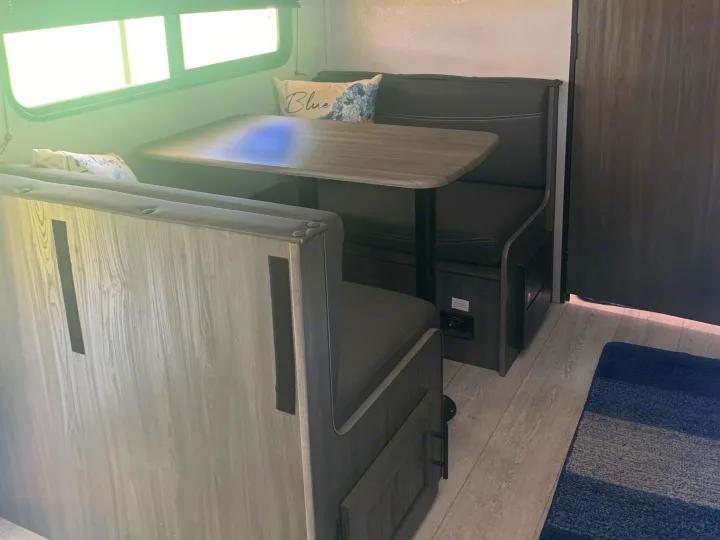 Inside an RV rental: a comfortable dinette with grey seating, wood table, overhead storage, and wall-mounted electronics.. Forest River Shasta 2021
