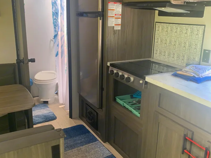 Inside this RV rental: compact kitchen with stove, microwave, fridge, and a small bathroom visible.. Forest River Shasta 2021