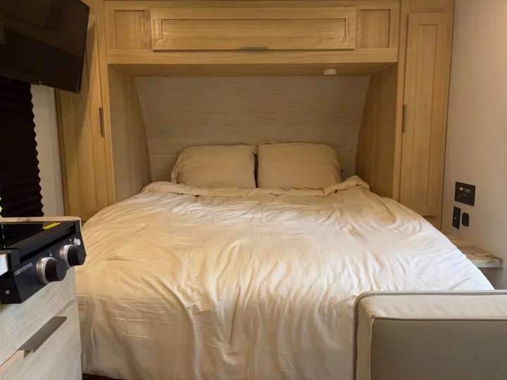 Compact RV rental bedroom featuring a full bed, overhead storage, and a built-in Greystone cooktop for versatile living.. Forest River Wildwood FSX Platinum 2023