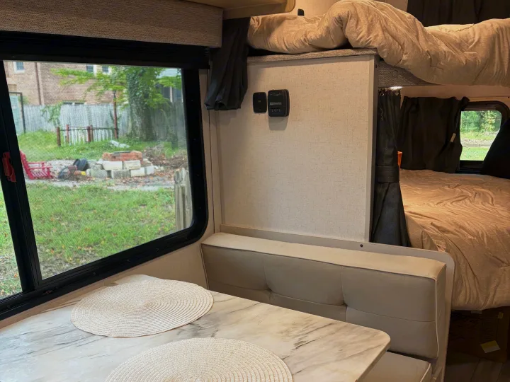 Spacious RV rental interior with a bright dinette, bunk beds, thermostat, and a large window showing a grassy outdoor scene.. Forest River Wildwood FSX Platinum 2023
