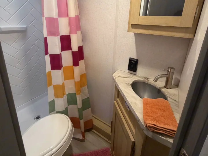 Compact RV rental bathroom featuring a toilet, colorful shower, and vanity with sink.. Forest River Wildwood FSX Platinum 2023