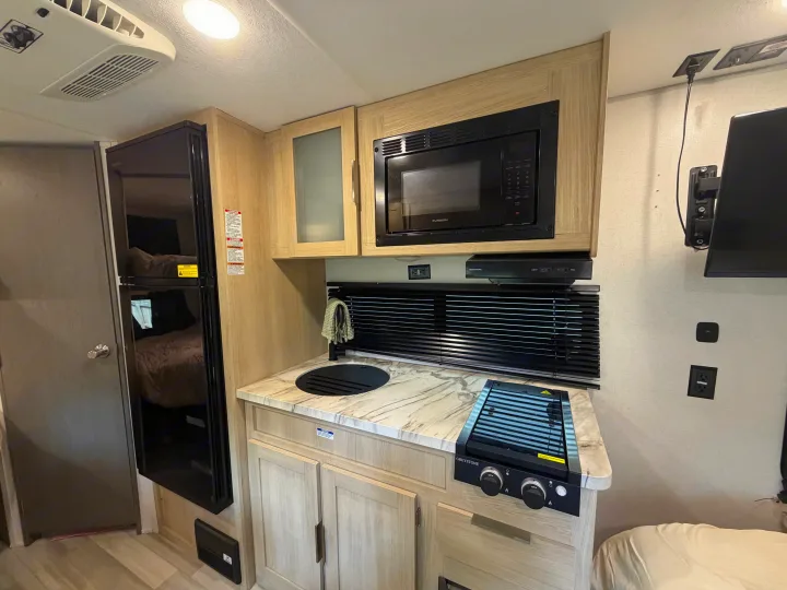 Inside this RV rental: a compact kitchen with microwave, fridge, stovetop, sink, plus visible bunks. Perfect for trips!. Forest River Wildwood FSX Platinum 2023