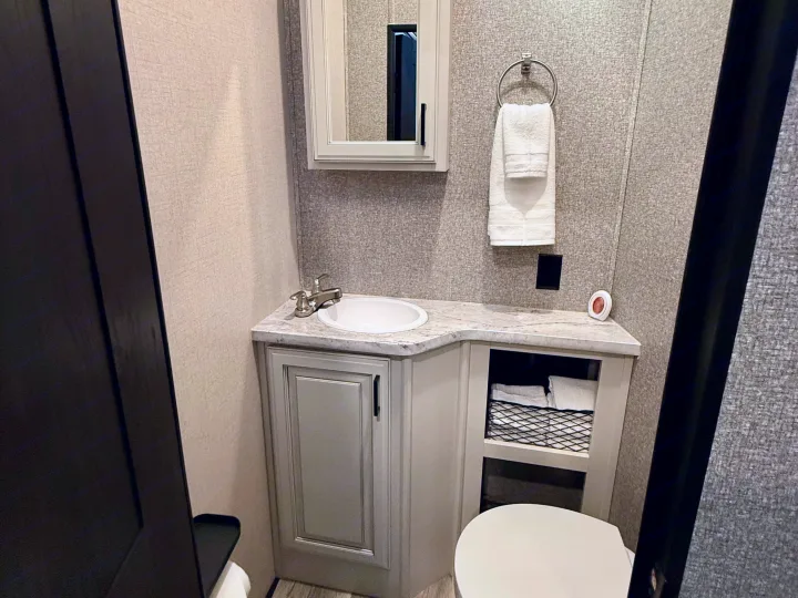 This RV rental bathroom features a compact vanity, sink, medicine cabinet, toilet, and fresh towels. Clean, modern design with textured walls.. Highland Ridge RV Open Range 2022