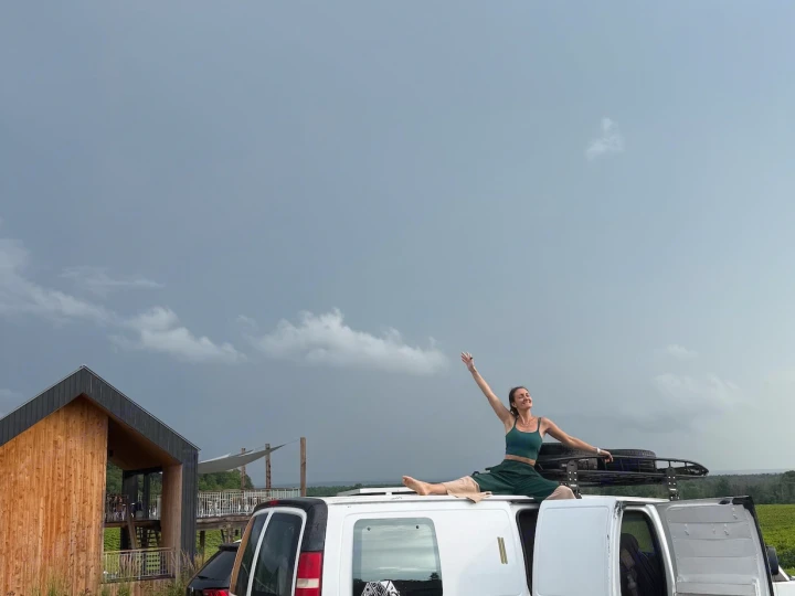 Woman doing splits on top of an rv rental van. Enjoying flexible travel and adventure with a modern building nearby.. Gmc Savanna C1500 2005