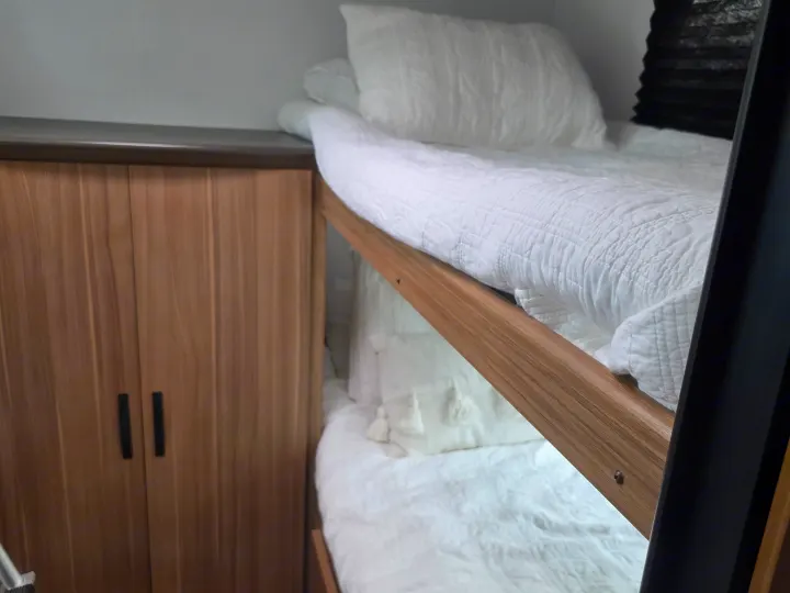 Inside a cozy RV rental: two neatly made bunk beds with white linens and wooden frames, next to storage cabinets.. Keystone RV Passport Classic 2025