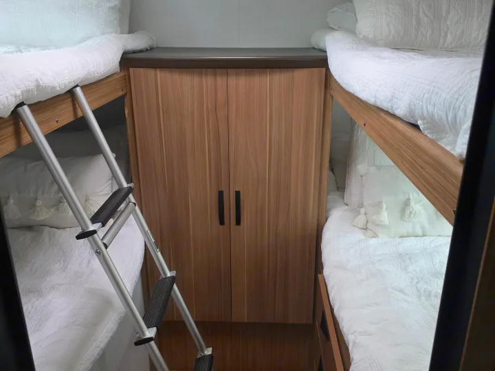 Compact RV rental: cozy bunk beds with crisp white bedding, a ladder, and a built-in wooden storage cabinet.. Keystone RV Passport Classic 2025