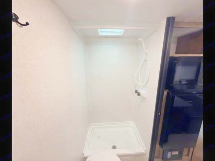 RV rental interior: compact bathroom with shower, toilet, next to kitchen with microwave & fridge. Bright white walls.. Keystone RV Springdale Mini 2025