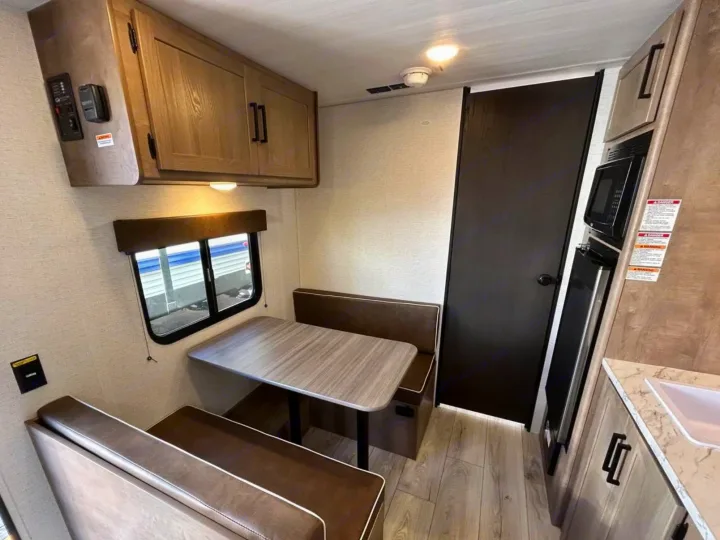 Inside this RV rental: dinette seating, table, overhead storage, window, and a compact kitchen with a microwave.. Keystone RV Springdale Mini 2025