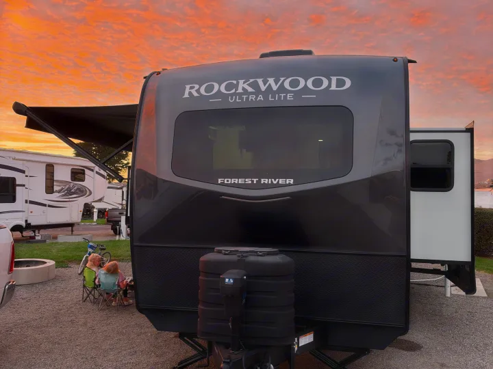 RV rental: Two kids relax by a Rockwood Ultra Lite travel trailer in an RV park, bathed in the glow of a beautiful sunset.. Forest River 2706BH 2026