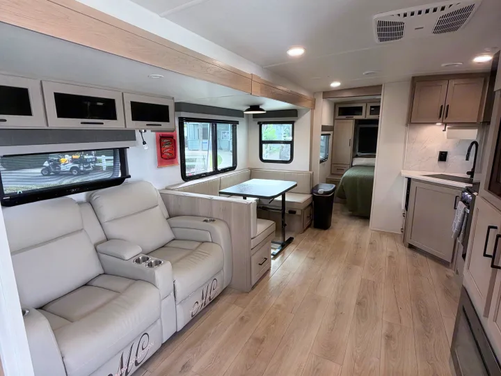 Spacious RV rental interior: light recliners, dining booth, kitchenette, and a cozy bedroom area with modern finishes.. Forest River 2706BH 2026