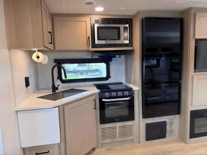 Modern RV rental kitchen interior with light wood cabinets, black appliances, a sink, stove, and microwave.. Forest River 2706BH 2026