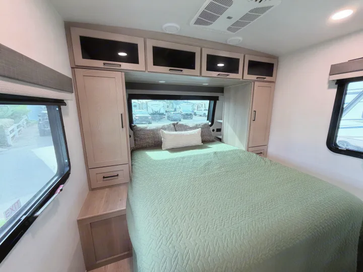 Comfortable modern RV rental bedroom featuring a green bed, overhead storage, and large windows. Your cozy home on wheels.. Forest River 2706BH 2026