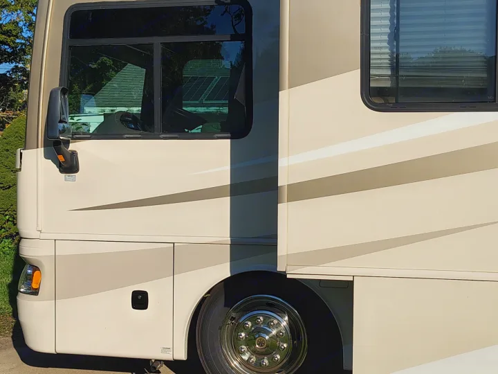 Side view of a beige RV rental with striped accents, chrome wheel, and solar panels reflected in the front window. Ready for your trip!. Fleetwood 38v 2008