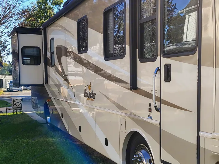 Exterior of a beige Bounder RV rental, a diesel motorhome with a slide-out extended and graphic stripes, parked on grass.. Fleetwood 38v 2008