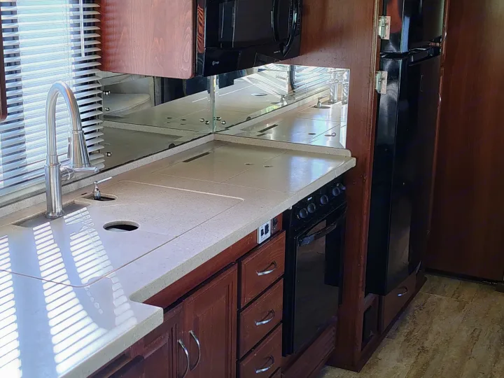Compact RV rental kitchen interior with sink, stove, microwave, and refrigerator. Mirrored backsplash reflects window blinds.. Fleetwood 38v 2008