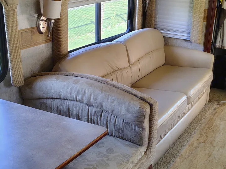 Cozy RV rental interior featuring a beige sofa, patterned dinette, and windows with outdoor scenery for your travels.. Fleetwood 38v 2008