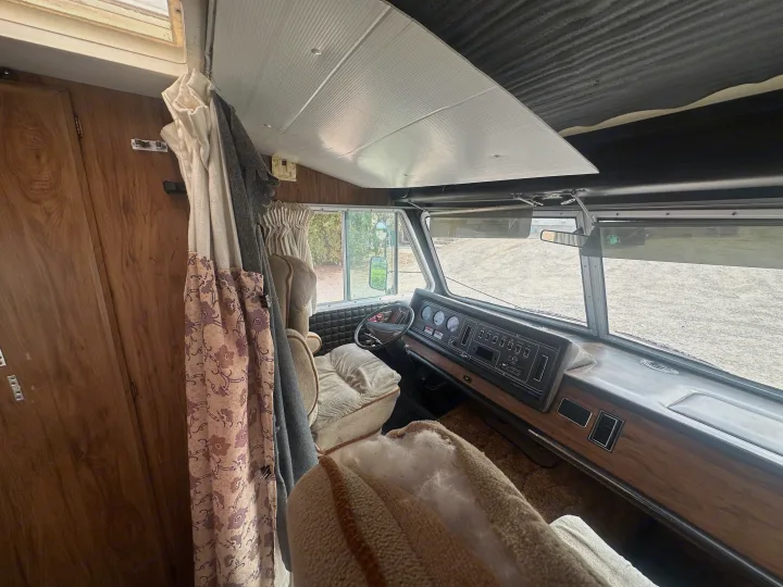 Vintage RV rental interior: cockpit view with dashboard, worn seating, curtains, and wood paneling.. Winnebago Winnebago 1980