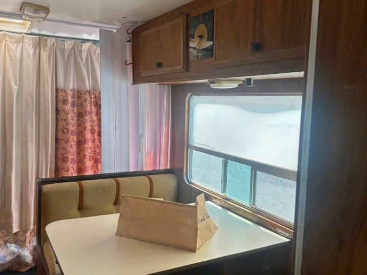 Cozy vintage rv rental interior with dining booth, wooden cabinets, and window. Patterned curtains add charm to this classic setup.. Winnebago Winnebago 1980