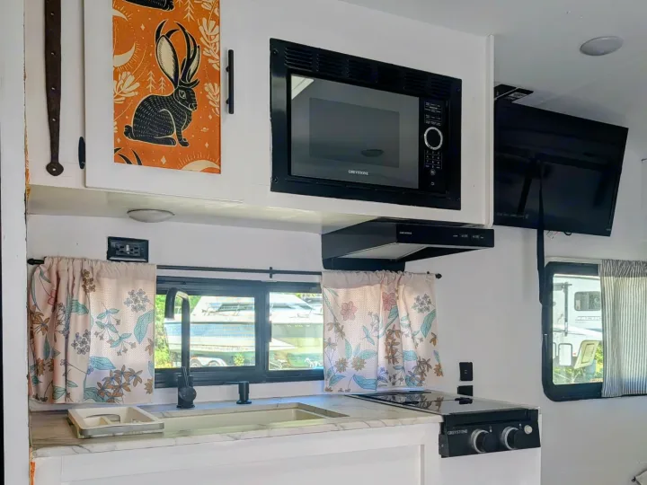 Modern RV rental kitchen featuring a microwave, stovetop, sink, and unique rabbit-themed cabinets. Ideal for travel.. Forest River Salem FSX Plantium 2022