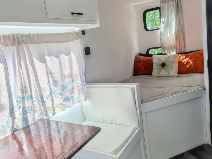 Bright RV rental: a cozy interior with a dinette, floral curtains, and a bed adorned with colorful pillows.. Forest River Salem FSX Plantium 2022
