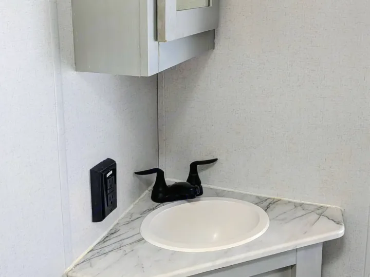 Compact RV rental bathroom with a white sink, black faucet, marble-look vanity, outlet, and light gray wall paneling. Efficient design.. Forest River Salem FSX Plantium 2022