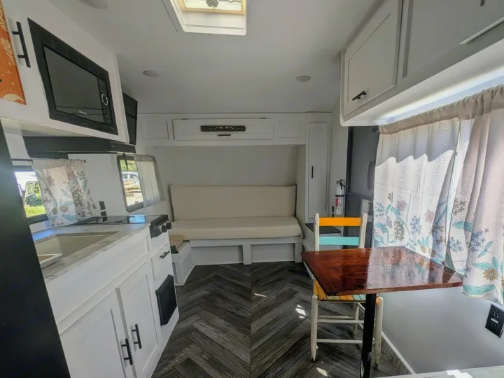 Clean RV rental interior: kitchen with microwave, bench seating, dining table, and patterned curtains.. Forest River Salem FSX Plantium 2022