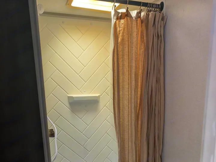 Compact, bright RV rental shower features white herringbone walls, built-in shelf, and a chic striped curtain.. Forest River Salem FSX Plantium 2022