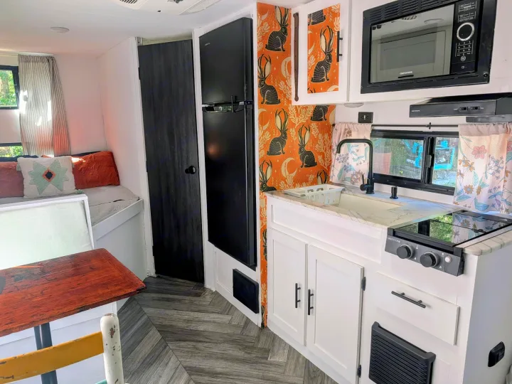 Inside a chic rv rental: Features a modern kitchen with black appliances, rabbit wallpaper, white cabinets, and herringbone flooring.. Forest River Salem FSX Plantium 2022