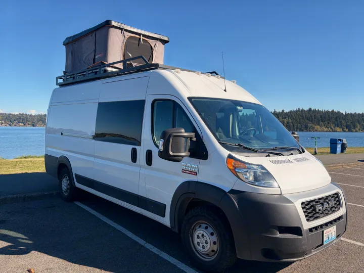 This white Ram ProMaster RV rental, featuring a Roofnest pop-top, is parked by a beautiful lake under a clear sky.. Dodge RAM Promaster 3500 2020