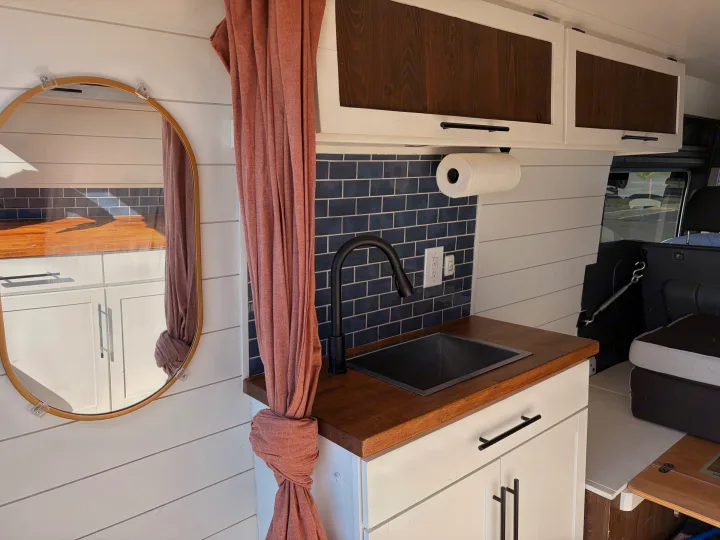 Inside an RV rental: a modern kitchenette featuring a sink, wood counter, blue subway tiles, and a decorative mirror.. Dodge RAM Promaster 3500 2020