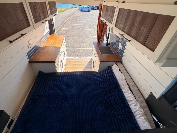 Explore this stylish rv rental camper van interior. Featuring a custom kitchen, comfy bed, and a scenic park view.. Dodge RAM Promaster 3500 2020