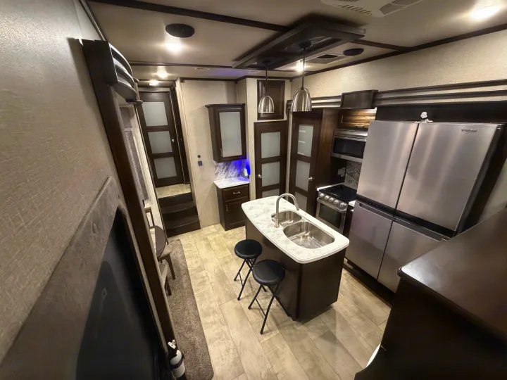 Well-equipped RV rental kitchen features a modern island, stainless steel appliances, and a cozy dining nook.. Grand Design Momentum Toy Hauler 2020