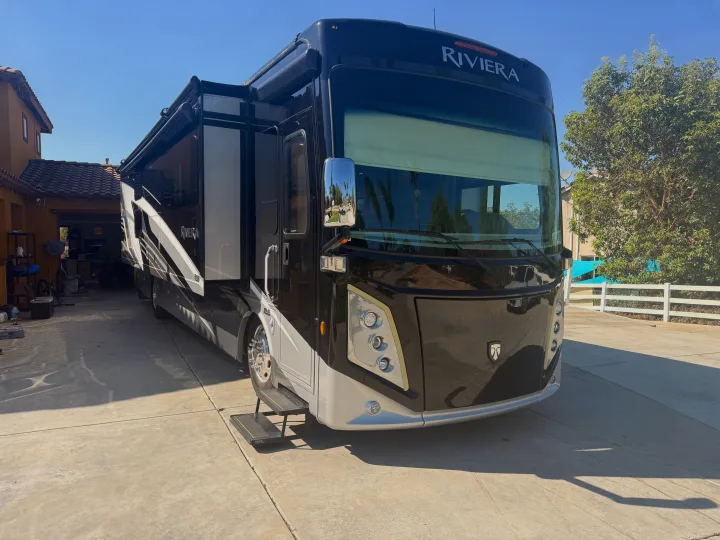 Luxury black & silver Riviera RV with slide-out & steps extended, parked on a sunny driveway, perfect for rv rental.. Thor Riviera 2024