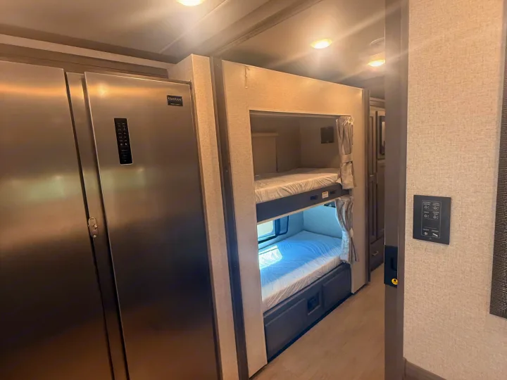 RV rental interior featuring a stainless steel refrigerator and cozy bunk beds with curtains, offering compact living space.. Thor Riviera 2024