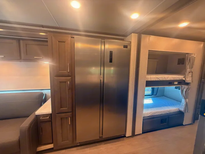 Spacious RV rental interior featuring a large stainless steel refrigerator, ample cabinetry, a comfortable sofa, and cozy bunk beds.. Thor Riviera 2024
