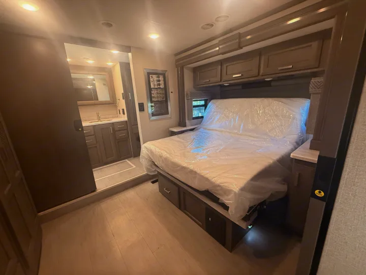 Explore this RV rental's bedroom, featuring a new bed with storage, overhead cabinets, and a connected bathroom with vanity.. Thor Riviera 2024