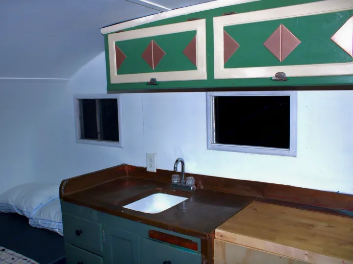 RV rental interior featuring custom green cabinets, a copper sink counter, and a compact sleeping area.. Shasta 1500 1954