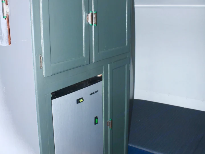 Compact rv rental interior with a grey-green cabinet, built-in mini-fridge, and nearby sleeping area.. Shasta 1500 1954