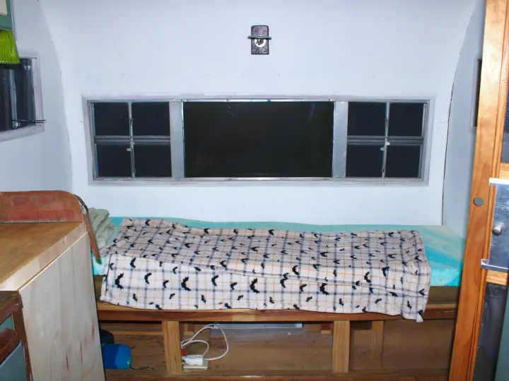 RV rental interior shows a sleeping area with multiple windows, a bed with a bat-patterned blanket, and basic amenities.. Shasta 1500 1954