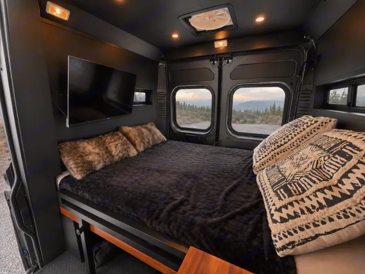 Dark and cozy RV rental bedroom with a plush bed, TV, and scenic mountain views from the windows, perfect for adventure.. Dodge Ram 1500 2020
