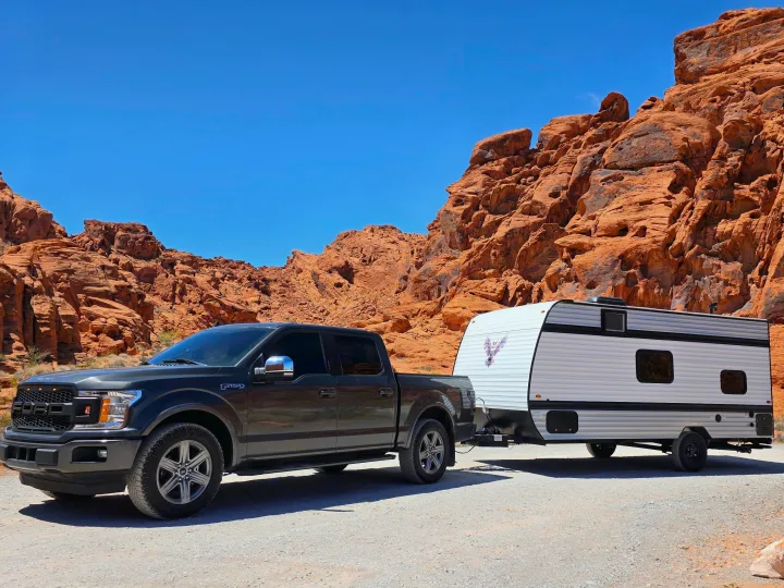 An F-150 truck tows an RV rental on gravel, set against stunning red rock formations under a bright blue sky.. Keystone Coleman 17B 2025