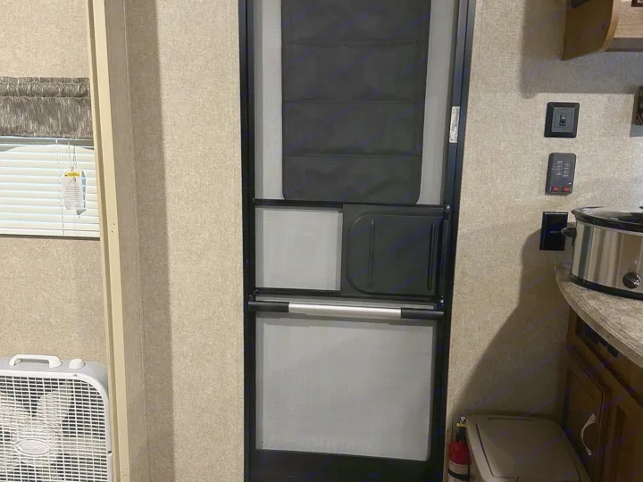 RV rental interior: A screen door with blackout blind, window, and fan on the left. Controls, slow cooker, and fire extinguisher on the right.. Coachmen Catalina 2017
