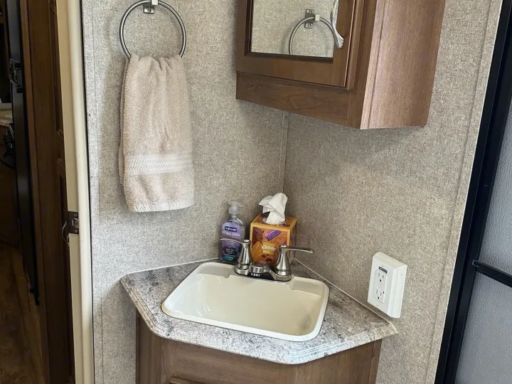 Compact RV rental bathroom with corner sink, soap, tissues, towel, and mirror cabinet.. Coachmen Catalina 2017