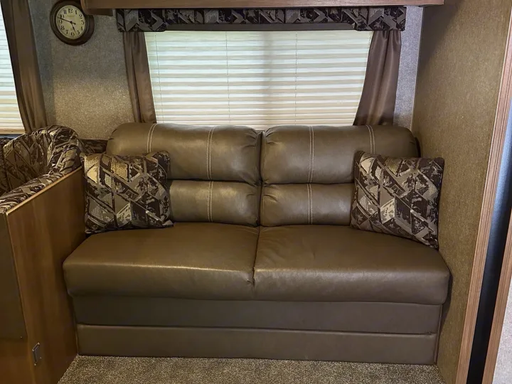 Comfortable RV rental living area with a brown faux-leather sofa, geometric pattern throw pillows, and blinds.. Coachmen Catalina 2017