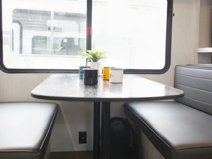 RV rental dinette: table with enamel mugs, a plant, and comfortable bench seating by a bright window.. Heartland Trail Runner 2022